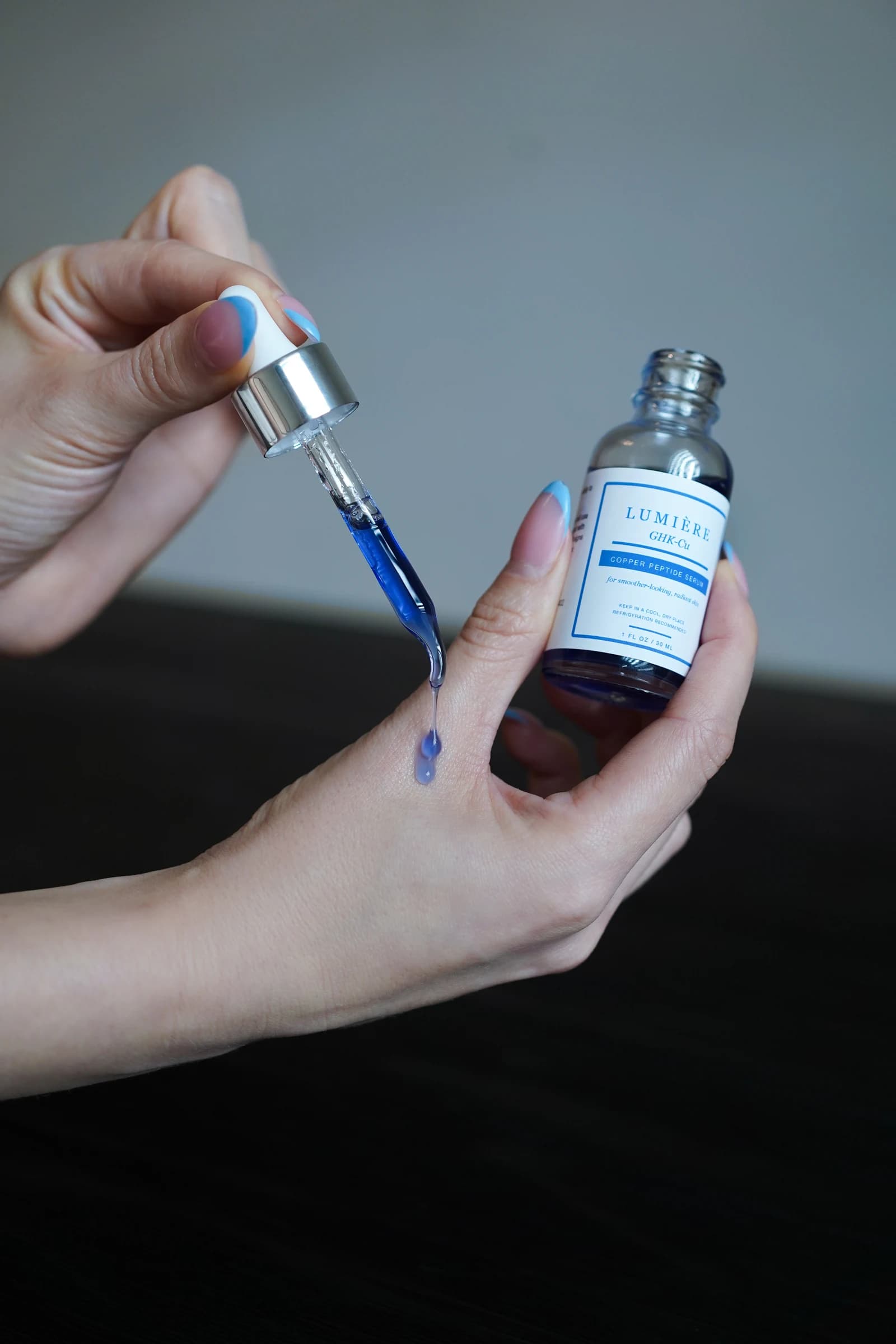 A blue serum drop held above the back of a hand