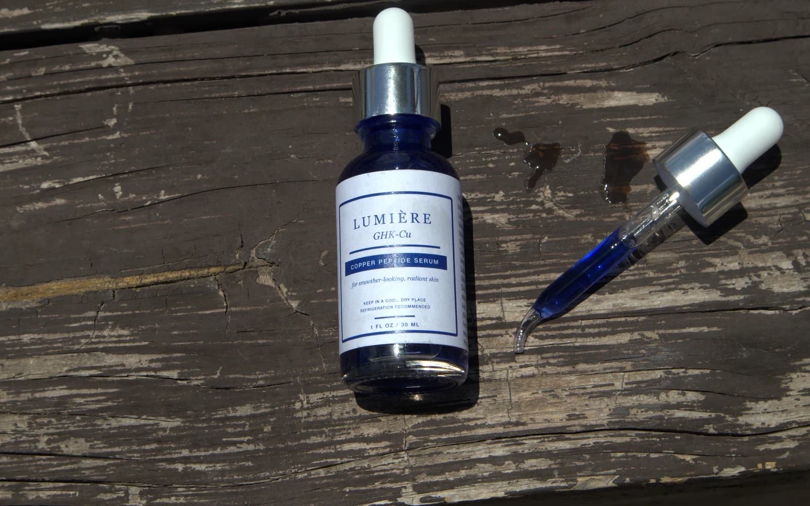 Authentic copper peptide serum and blue-filled dropper on sunlit weathered wood