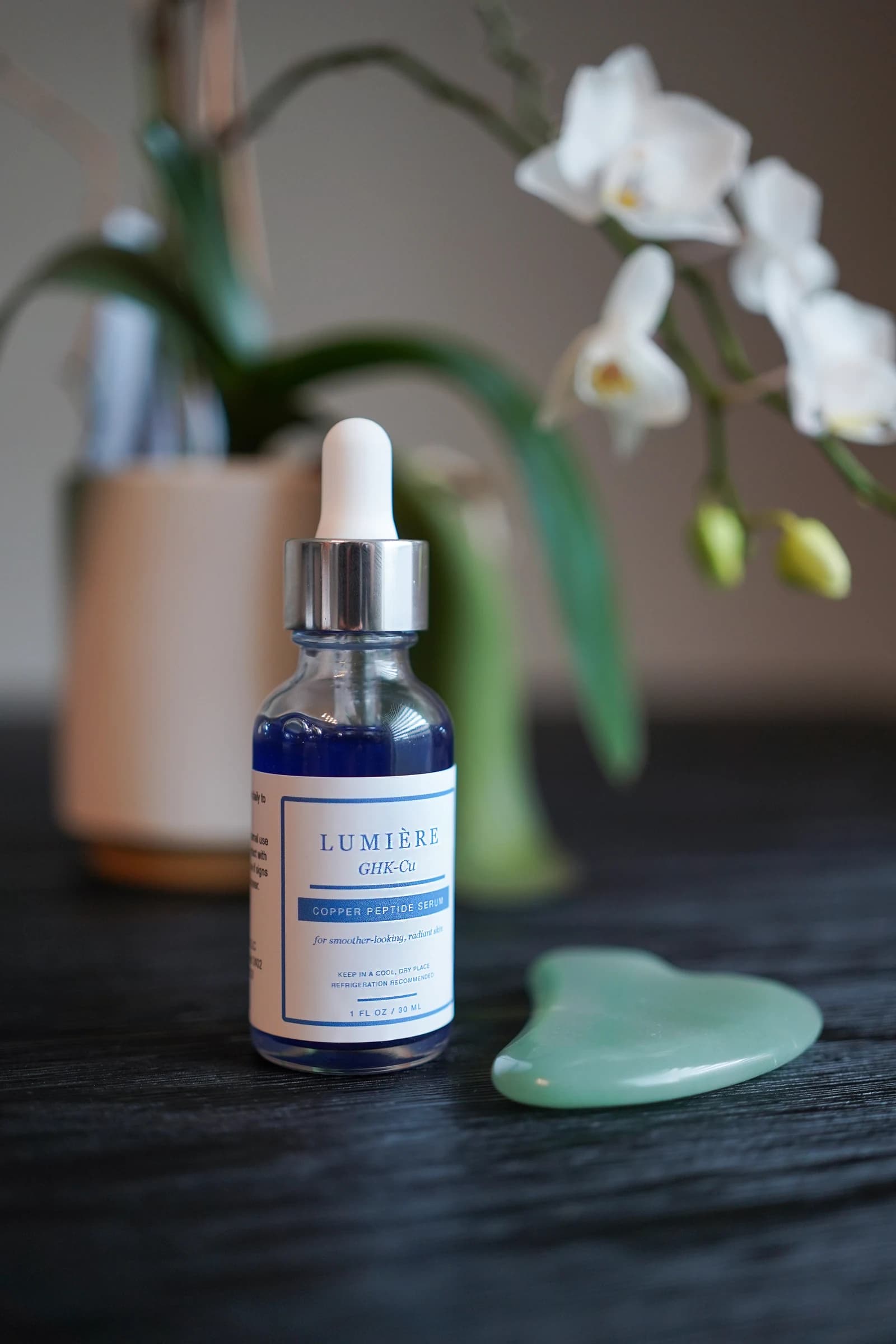 Lumiere Routine serum beside an orchid in a skincare still life