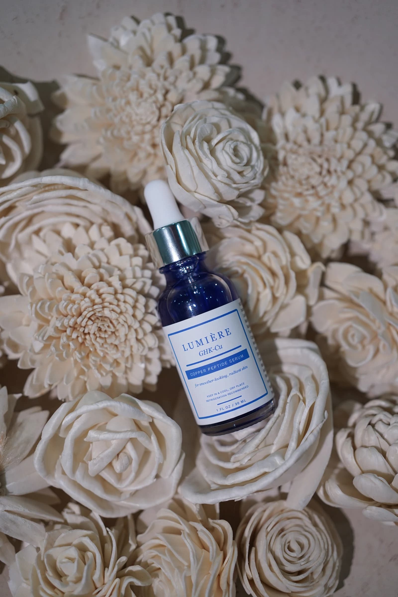 Lumiere Routine serum resting among sculptural cream flowers